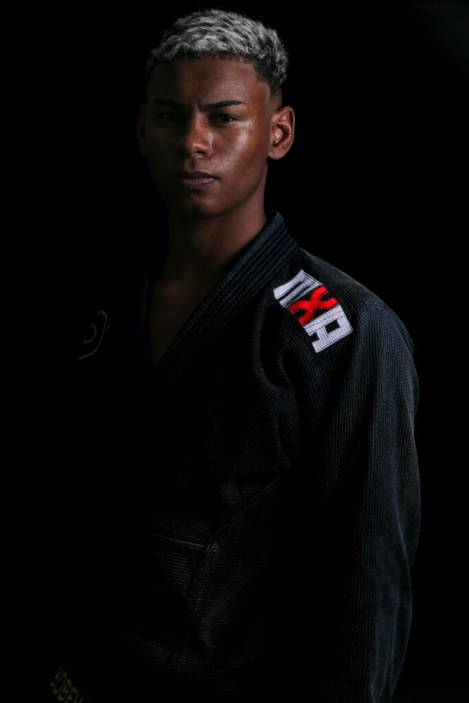 Confident martial artist in black gi with embroidered logo on black background.